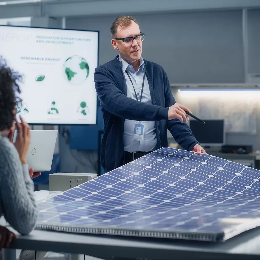 Employees in office around a flexible solar panel, with plans in the background