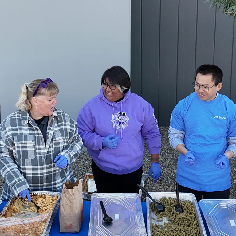 Diverse people outside, wearing coats, in front of trays of food ready for distribution